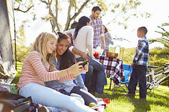 Two Girls Using Mobile Phone On Family Camping Holiday
