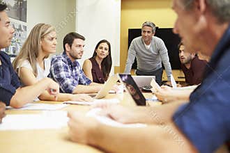 Male Boss Addressing Meeting Around Boardroom Tabl