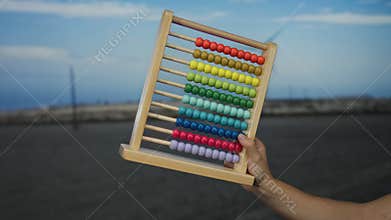 Hand holding colorful abacus outdoors in front of windmill and landscape during day