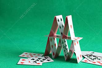 Collapsed house of playing cards on green background. Space for text