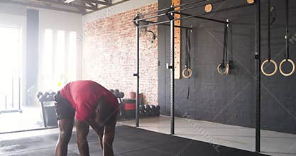 African American male gripping rope at gym squatting swinging it then crouching catching breath