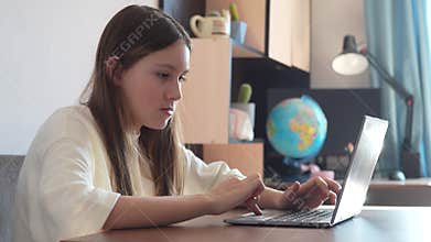 Girl is using a laptop for education. girl is studying remotely at home. girl in white blouse is doing her homework on laptop