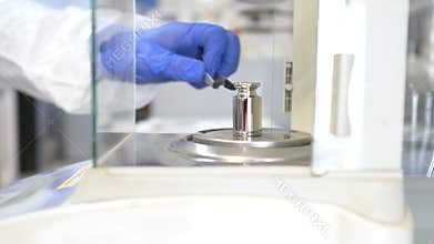 A operator's hand is holding steel calibration weight to place on the analytical balance.