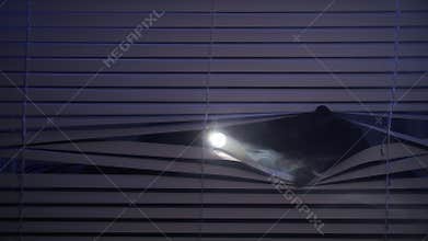 robbery, man in balaclava shines flashlight through blinds at night looking for cheap items, close-up