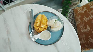 Mango Sticky Rice Dessert Served on a Blue Plate With a Spoon and Fork in a Cozy Cafe Setting. Top view
