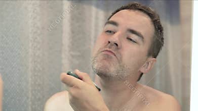 young man shaving his beard with electric shaver. He shaved half of beard.