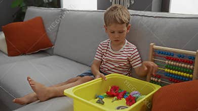 Blond boy playing with toys and an abacus on a couch in a comfortable living room