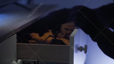 burglar wearing gloves rummaging through clothes rack looking for valuables at night in house, close up