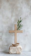 Wooden cross with olive branch and bowl on stone against textured wall