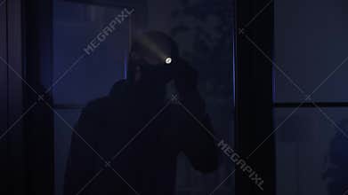 crime and criminality, man in a balaclava illuminates a room with a flashlight in search of valuables