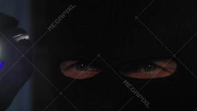 robbery and burglary, man in balaclava with flashlight in hands looks around in dark room, close-up