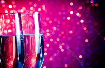 Champagne flutes with gold bubbles on blue and violet tint light bokeh background