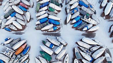 Camera panning over sailboats covered in snow, aerial drone view. Frozen sailboats storage