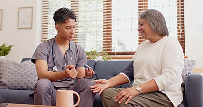 Male nurse checking blood pressure of senior woman on couch at home