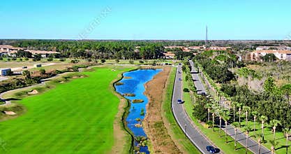Drone footage of blue lake next to the road surrounded by greenery on a sunny day with blue sky