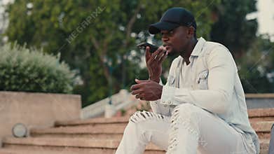 Young african american man using hands free mode on phone sitting in urban park.