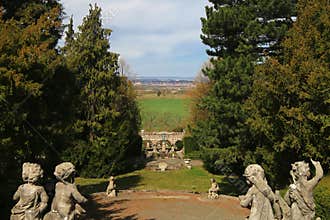 Statues framing Roseburg garden view in Germany, with distant town beyond green fields and formal tree borders