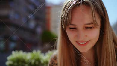 Blonde woman resting at urban table, soft bangs framing peaceful expression, basking in warm daylight with delicate, contemplative