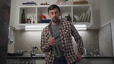 Young man, drunk and alone in the kitchen at night, clutches an empty wine bottle. He speaks to himself, consumed by