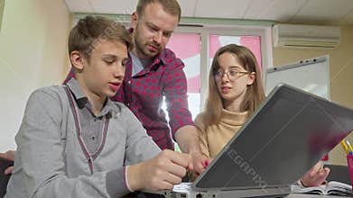 Mature male teacher guiding students through an assignment using a laptop