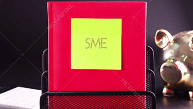 Animation of text SME, abbreviation of Small and Medium Sized Enterprise on a bright red book with a sticker note attached on a