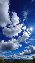 Brilliant Sun Shining Through Fluffy White Clouds on a Deep Blue Sky Above Rolling Hills with Green Vegetation on a