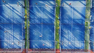Aerial view of three vibrant blue padel courts, captured by a drone. Several players are actively engaged in padel