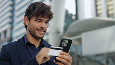 Portrait of Hispanic man uses smartphone and credit card for transaction outdoor