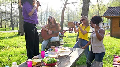 Four cheerful female friends singing and dancing at a picnic