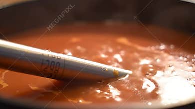 Food Thermometer Probing Simmering Orange Sauce in Black Pot Close Up