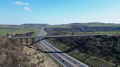 Arched concrete bridge spans across a busy multilane highway running through rolling green hills