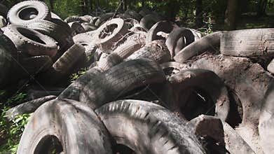 A large pile of old tires accumulates in a wooded location, posing environmental risks. Debris surrounds the area