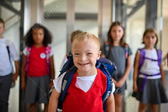 Boy with down syndrome among schoolkids in uniforms, standing in school corridor.