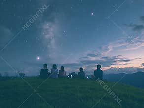 A serene nature scene on National Day Unplugging, with a group of people sitting on a grassy hill, gazing at the stars, phones put