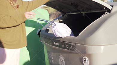 a woman throws garbage in a plastic bag into a waste bin on the street.