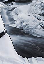 Icy river cascades through a frozen landscape, surrounded by thick snow and frost-covered rocks