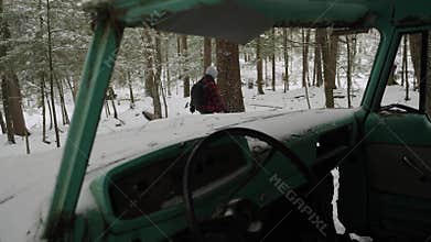 View of a Caucasian man hiking in winter in a forest through an old rusted abandon classic truck