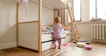 Adorable toddler girl playing near bunk bed in bedroom