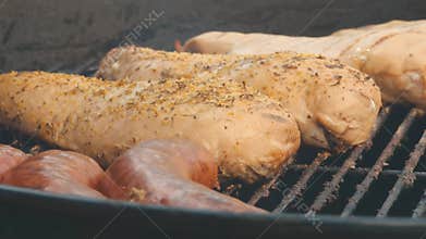 Closeup footage of grilling sausages and marinated chicken breasts on a charcoal grill