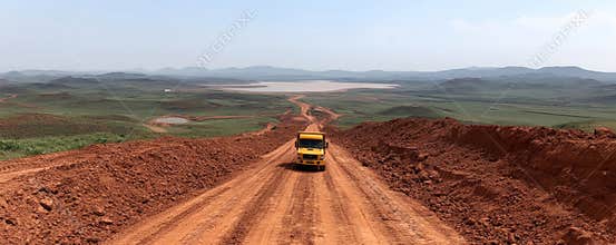 Mining truck hauling bauxite across rugged, rust colored terrain, kicking up dust while transporting mineral load