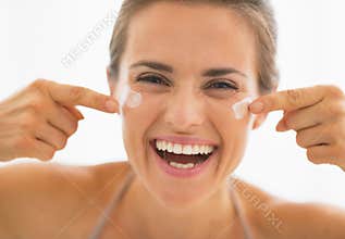 Happy woman having fun time while applying cream in bathroom