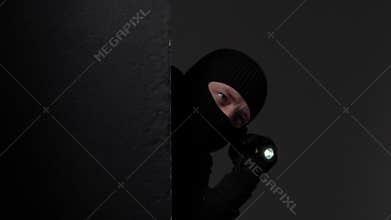 Masked intruder holding flashlight in darkness