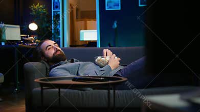 Upbeat homeowner laying down on couch watching feel good movies on TV