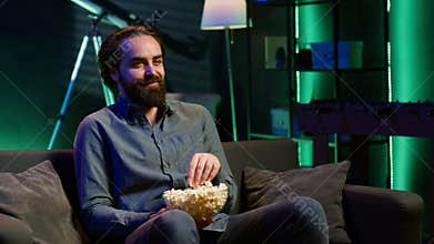 Man laughing at funny shows on television, eating snack, sitting on couch