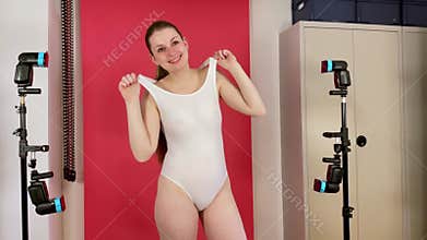 Pretty young woman in white swimsuit is posing in studio with pink background