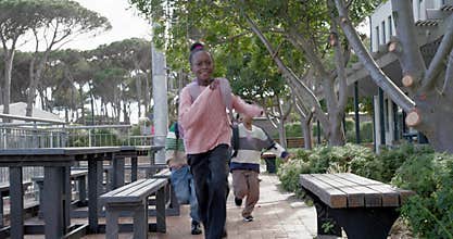 Diverse school-age children emerging from distance, running toward camera with backpacks to school