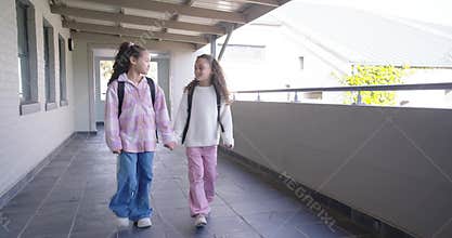 African American preteen girls entering corridor, walking holding hands toward class with backpacks
