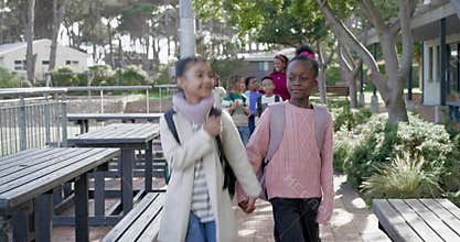 African American girls holding hands walking campus walkway leaving school with backpacks