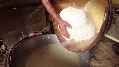 Hand presses the sheep cheese in a wooden tub on the background of a bonfire