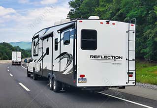 Pennsylvania, U.S.A - Jul 19, 2026 - A white Reflection fifth-wheel RV towed by pickup truck, featuring ladder, graphics, windows